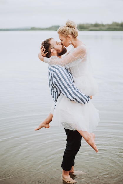 Young just married kissing and hugging on the shoreline.