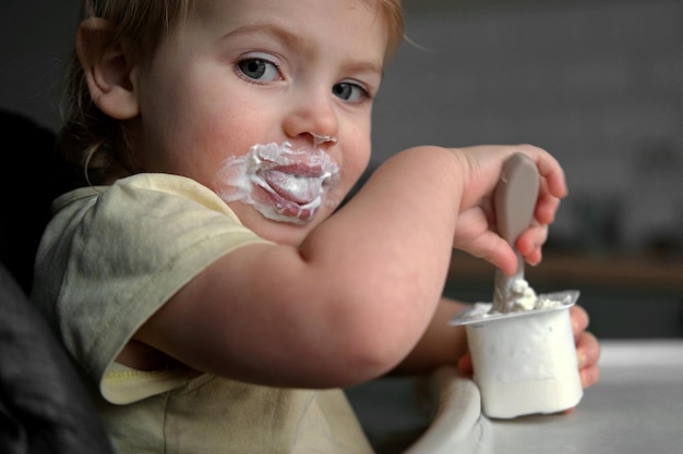 高い椅子に座って混ぜたマッシュを食べている幼い子供離乳中の幼い女の子が食べることを学んでいる