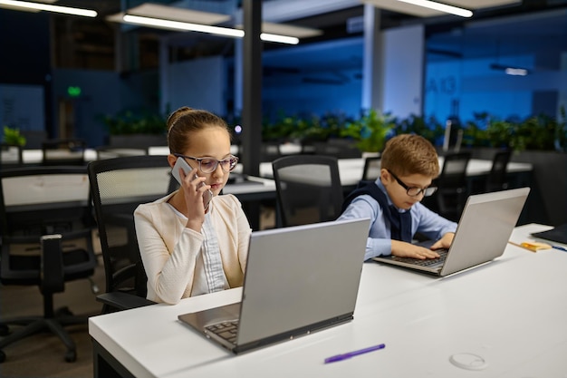 young kids designer working sitting at desk at office. little girl talking phone, boy using laptop