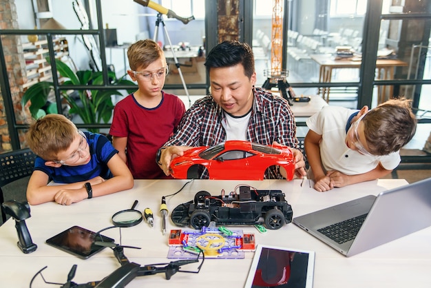 Young Korean man of electronics engineer with young children using screwdriver to disassemble robotic machine at the table in the modern school. Slow motion