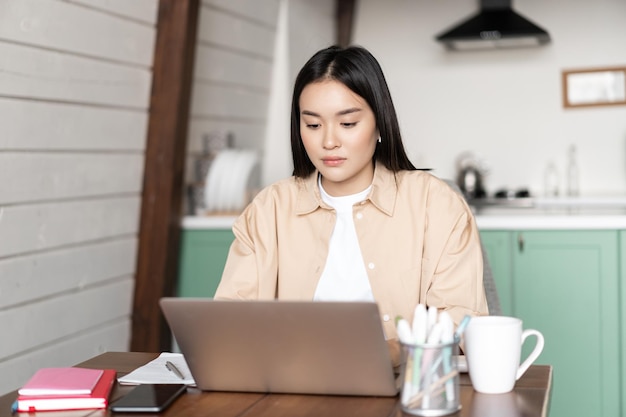 Young korean woman working on laptop from home girl writing on computer keyboard studying online or ...