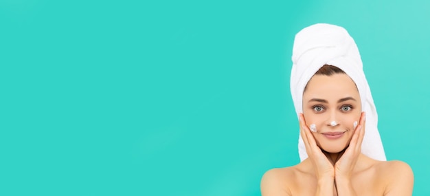 young lady apply face cream on blue background with copy space