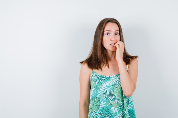 Young lady biting nails in blouse and looking stressed , front view.