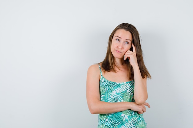 Young lady in blouse standing in thinking pose and looking pensive , front view.