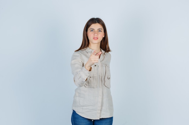 Young lady in casual, jeans pointing at front and looking confident , front view.