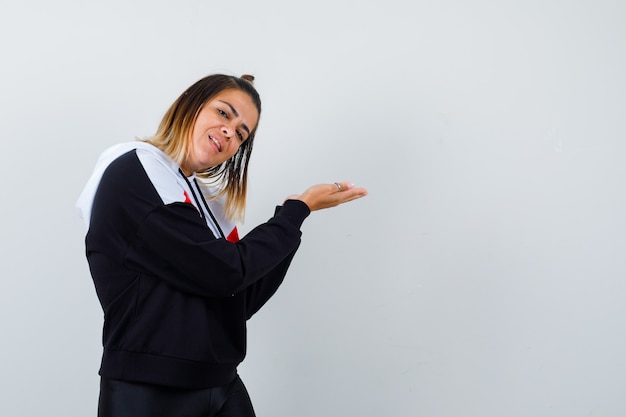 Young lady doing welcome gesture in hoodie sweater and looking pleased.