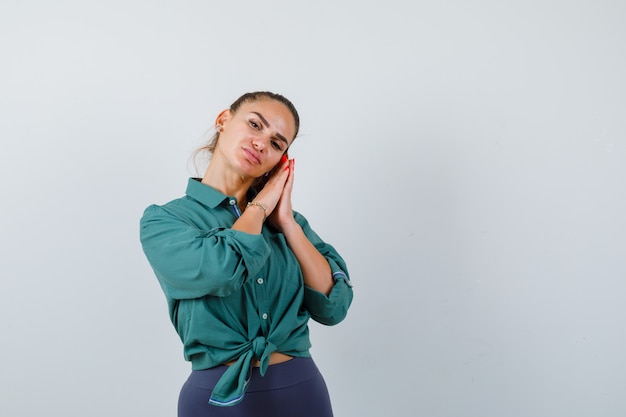 Foto giovane donna in camicia verde che si appoggia sui palmi come cuscino e sembra calma, vista frontale.