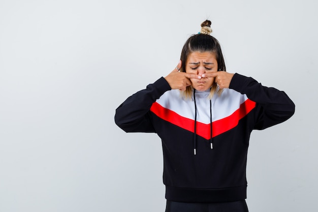 Young lady in hoodie sweater squeezing her pimple on nose and looking disappointed