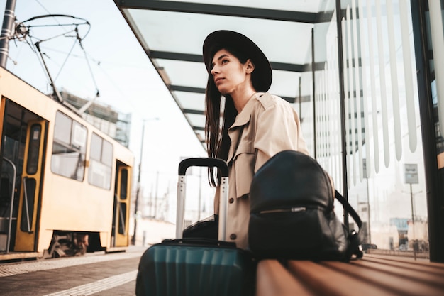 写真 コートと帽子の若い女性がバスのシティストップに座っています。