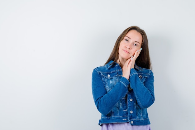 Giovane donna appoggiata sui palmi come cuscino in t-shirt, giacca e dall'aspetto sensato. vista frontale.