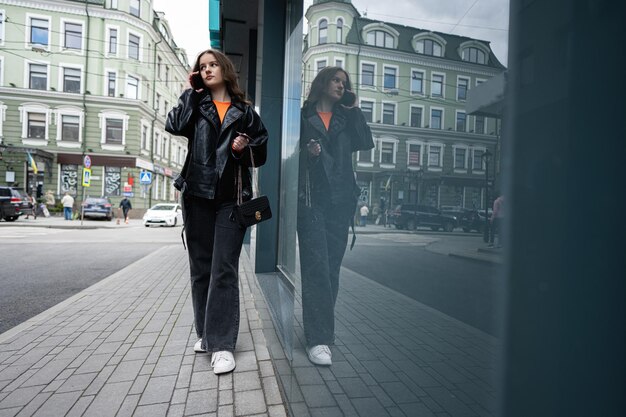 Young lady in leather jacket walking in urban city speaking on phone