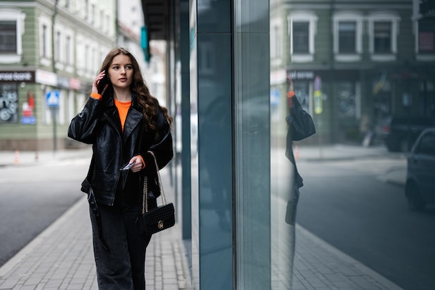 Young lady in leather jacket walking in urban city speaking on phone