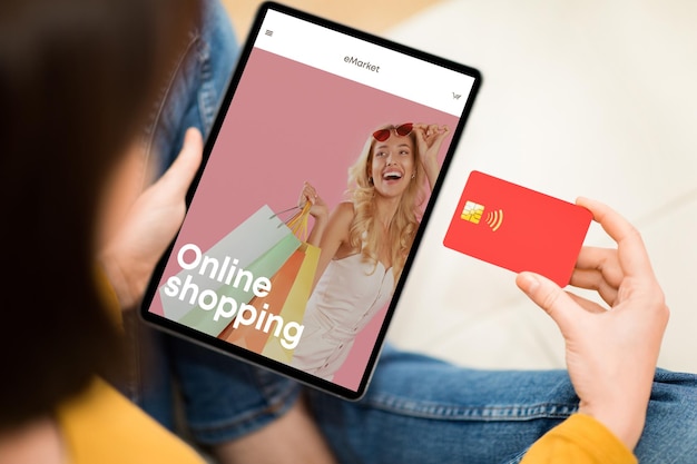 Young lady look at fashion store at tablet screen use credit card for buy new clothes with app