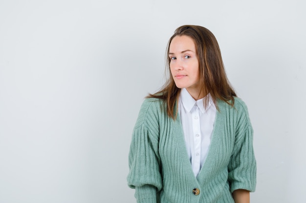 Giovane donna che guarda davanti in camicia, cardigan e sembra concentrata, vista frontale.