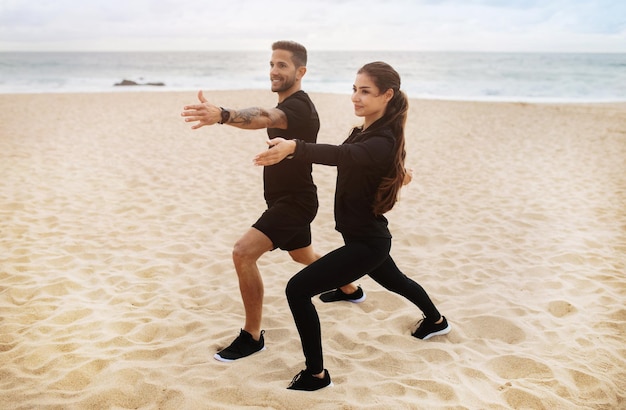 Young lady and man in sportswear doing stretching practice yoga on ocean beach enjoying workout full