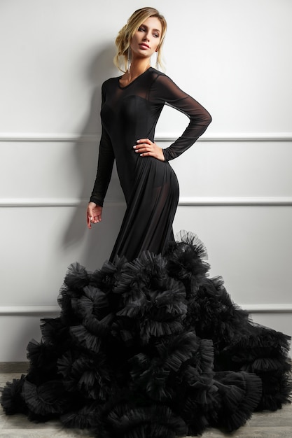 ファッションの長い黒のドレスでポーズをとる若い女性