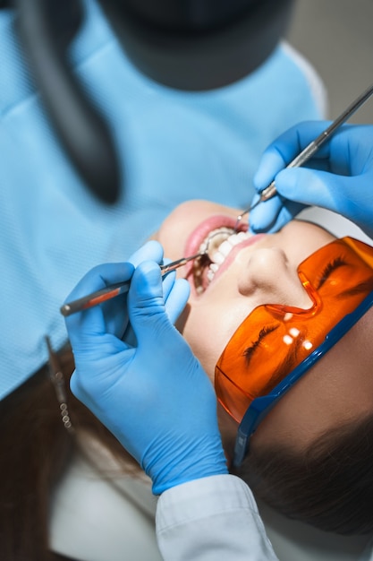 Young lady in protective glasses is lying in dental chair while doctor is examining her with mirror and explorer