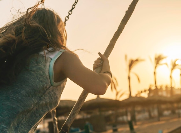 Young lady riding on a swing at sunset on a background of palm trees