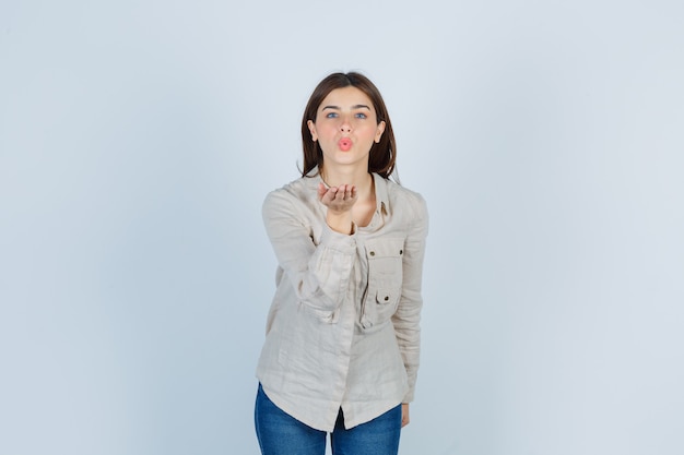 Young lady sending air kiss with pouted lips in casual, jeans and looking sincere. front view.