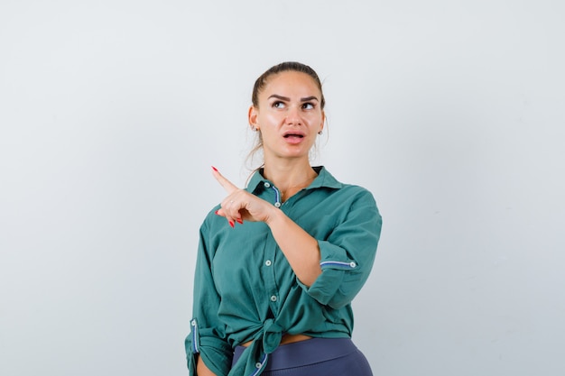 Young lady in shirt, pants pointing up and looking thoughtful , front view.