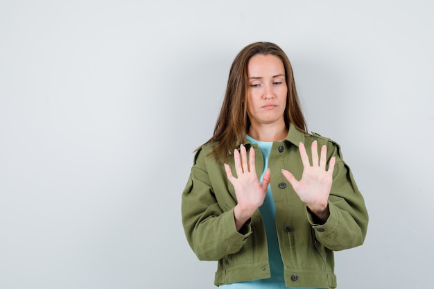 Young lady showing palms in t-shirt, jacket and looking serious. front view.