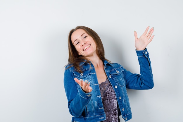 Giovane donna che mostra il segno di taglia in camicetta, giacca di jeans e sembra allegra, vista frontale.