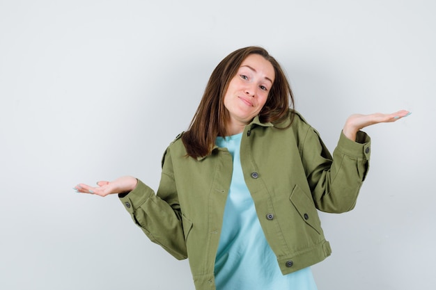 Young lady spread palms aside in t-shirt, jacket and looking happy , front view.