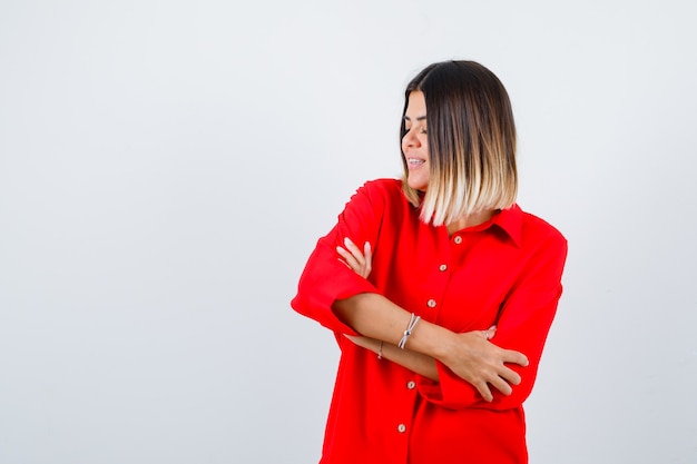 Young lady standing with crossed arms in red oversize shirt and looking pleased , front view.