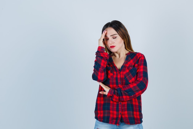 Giovane donna che soffre di emicrania in camicia a quadri e sembra infastidita. vista frontale.