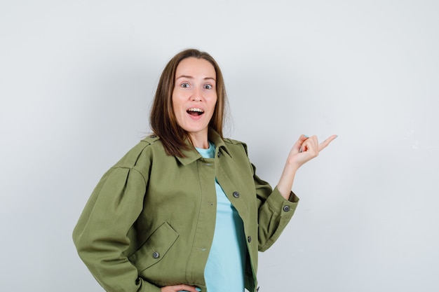 Giovane donna in t-shirt, giacca che punta verso il lato destro e sembra stupita, vista frontale.