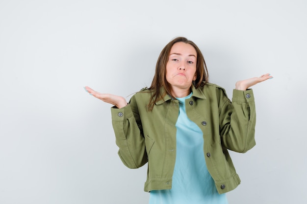 Young lady in t-shirt, jacket showing helpless gesture and looking clueless , front view.