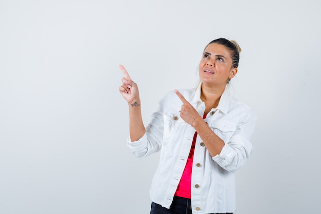 Young lady in t-shirt, white jacket pointing at upper left corner and looking focused , front view.