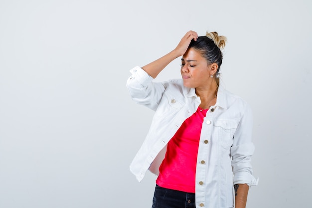 Young lady in t-shirt, white jacket with hand on head and looking forgetful , front view.