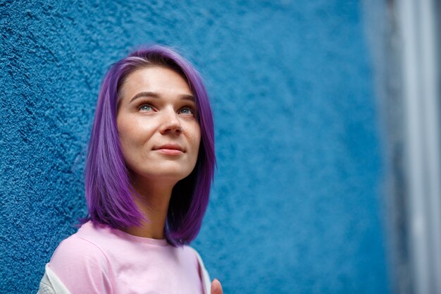 Young lady with bright violet hair grey eyes and pierced nose, looking up