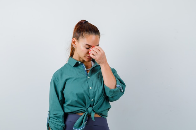 Young lady with hand on face, looking down in shirt, pants and looking puzzled , front view.