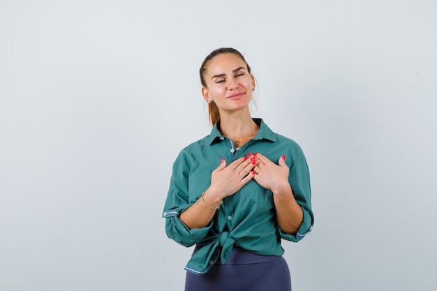 Young lady with hands on chest in green shirt and looking delighted , front view.