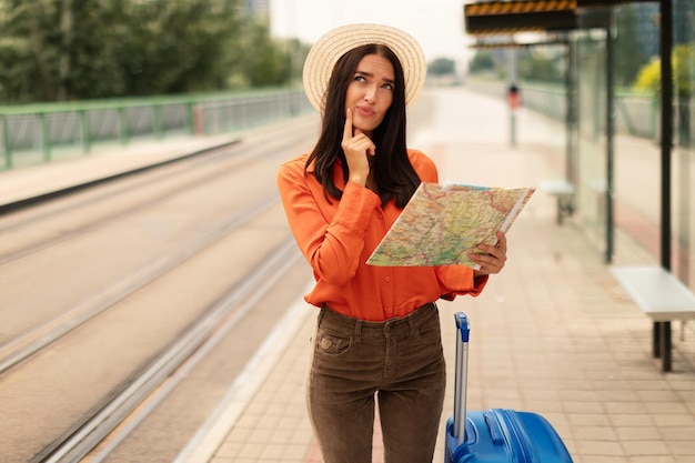 Young lady with map and suitcase waiting at tram stop