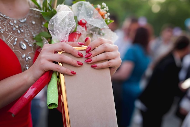 Young lady with red evening dress holding a bouquet of flowers leaned to the chair back