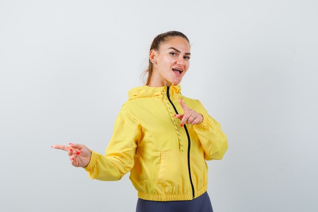 Young lady in yellow jacket pointing aside and looking cheery , front view.