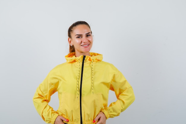 Young lady in yellow jacket with hands on waist and looking optimistic , front view.