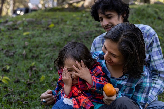 Young Latin American family sitting on the grass spending the afternoon in the park and playing with their 3 year old child Family concept