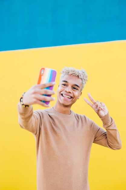 黄色と青の背景にスマートフォンで自分撮りをしている若いラテンアメリカ人男性