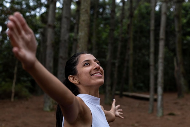 Молодая латиноамериканка 25 лет в сосновом лесу с распростертыми объятиями к небу празднует свободу Концепция положительных человеческих эмоций и восприятия жизни