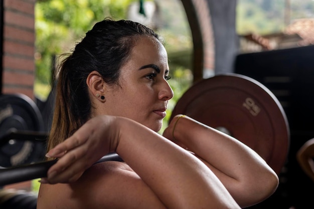 Young Latin American woman standing holding on her shoulders a barbell with weights functional workouts performed at high intensity in the gym Healthy Lifestyle Concept