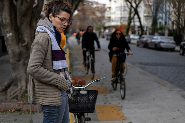 젊은 라틴 아메리카 여성이 자전거 타는 사람들이 지나갈 때 자전거 도로 옆에서 기다립니다.