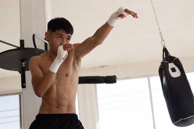 Young latin boxer training by throwing punches in the air\
inside a gym with discipline and determination his face is\
concentrated