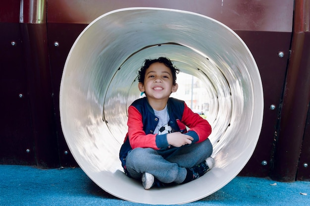 young latin boy inside plastic tunnel playing in park happy