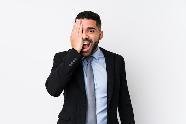 Young latin business woman against a white surface isolated having fun covering half of face with palm.