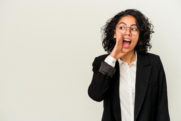 Young latin business woman isolated on white background is\
saying a secret hot braking news and looking aside