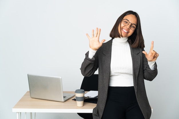 손가락으로 7 세 흰색 배경에 고립 된 사무실에서 일하는 젊은 라틴 비즈니스 여자